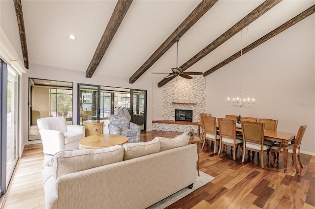 living room with high vaulted ceiling, ceiling fan with notable chandelier, a stone fireplace, beamed ceiling, and light hardwood / wood-style floors