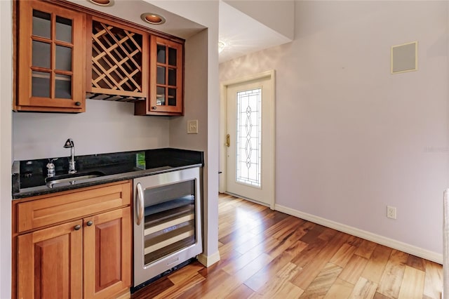 kitchen with light hardwood / wood-style floors, dark stone countertops, sink, and beverage cooler