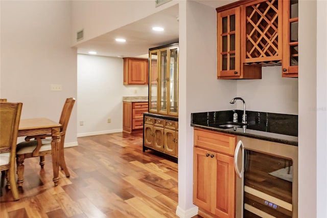 kitchen with wine cooler, dark stone countertops, light wood-type flooring, and sink