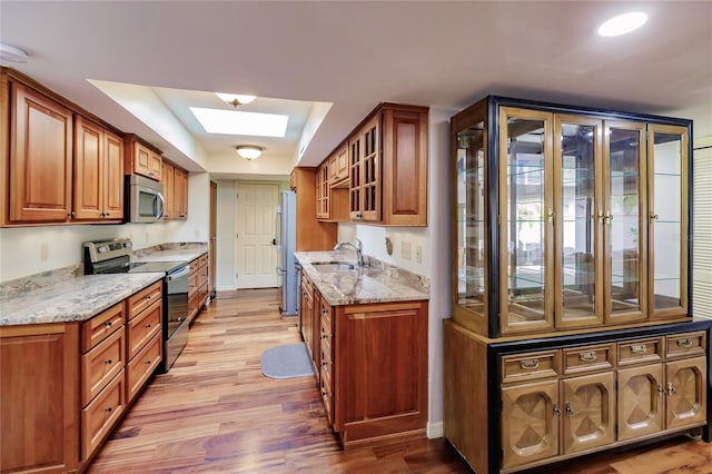 kitchen featuring appliances with stainless steel finishes, light wood-type flooring, a skylight, light stone counters, and sink