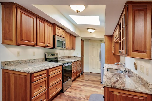 kitchen with appliances with stainless steel finishes, light wood-type flooring, a skylight, light stone counters, and sink