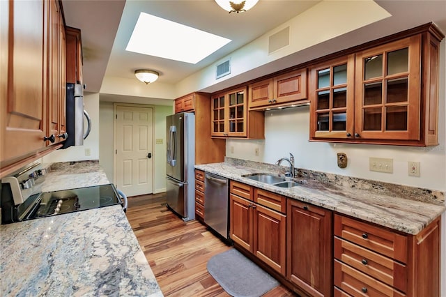 kitchen with sink, a skylight, light wood-type flooring, light stone countertops, and appliances with stainless steel finishes