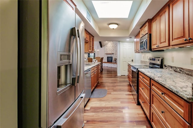 kitchen featuring light stone countertops, a skylight, a brick fireplace, stainless steel appliances, and light hardwood / wood-style flooring