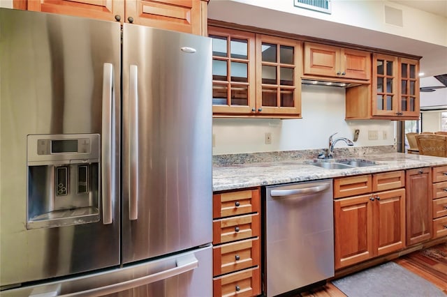 kitchen featuring stainless steel appliances, light stone counters, light hardwood / wood-style floors, and sink