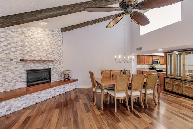 dining area with ceiling fan with notable chandelier, beam ceiling, hardwood / wood-style flooring, high vaulted ceiling, and a fireplace