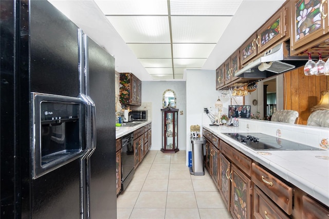 kitchen with light tile patterned flooring, dark brown cabinets, tile counters, and black appliances