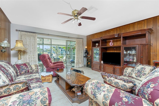 tiled living room featuring ceiling fan and wood walls