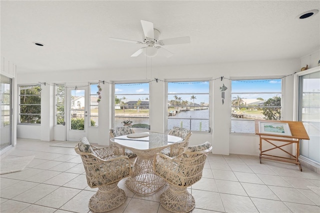 sunroom with ceiling fan and a water view