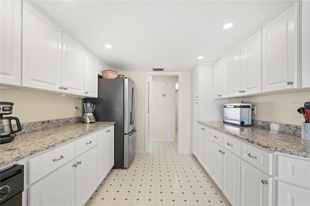 kitchen with white cabinets, stainless steel fridge, and light stone counters