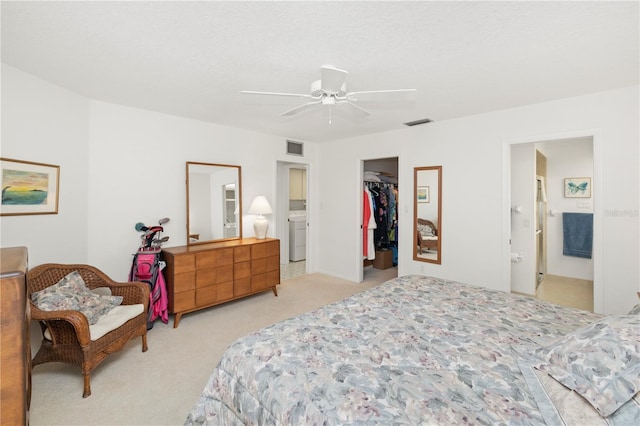 carpeted bedroom featuring ceiling fan, ensuite bath, a closet, a walk in closet, and washer / clothes dryer