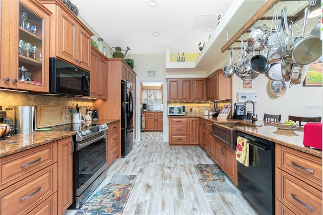 kitchen featuring sink, black appliances, light wood-type flooring, light stone countertops, and backsplash