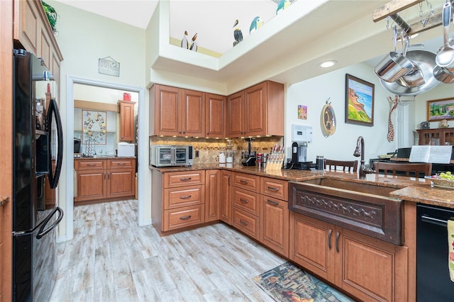 kitchen with stone countertops, tasteful backsplash, sink, light hardwood / wood-style floors, and black refrigerator with ice dispenser