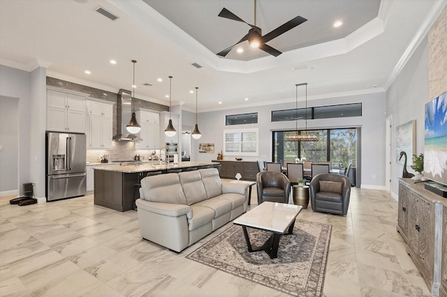 living room with ceiling fan with notable chandelier, a tray ceiling, and ornamental molding