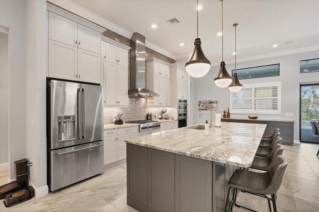 kitchen with pendant lighting, a spacious island, wall chimney exhaust hood, light stone counters, and stainless steel appliances