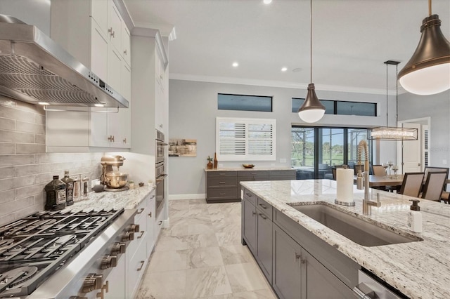 kitchen with appliances with stainless steel finishes, light stone counters, wall chimney range hood, white cabinetry, and hanging light fixtures