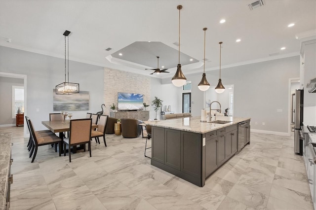 kitchen featuring light stone counters, sink, decorative light fixtures, and a center island with sink