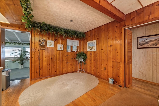 unfurnished room with light hardwood / wood-style floors, wooden walls, and beam ceiling