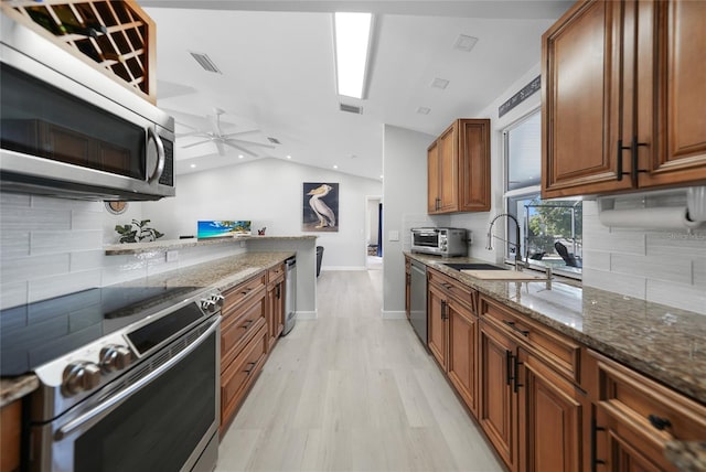 kitchen with sink, stainless steel appliances, dark stone countertops, light hardwood / wood-style floors, and vaulted ceiling