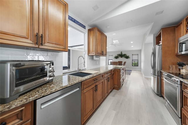 kitchen with sink, stainless steel appliances, lofted ceiling, stone countertops, and light wood-type flooring