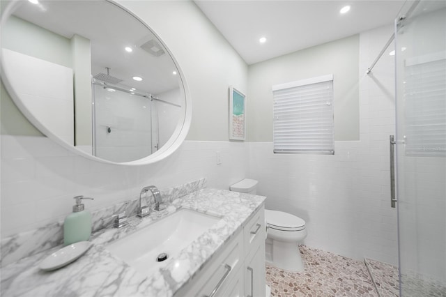 bathroom with vanity, toilet, a shower with shower door, and tile walls