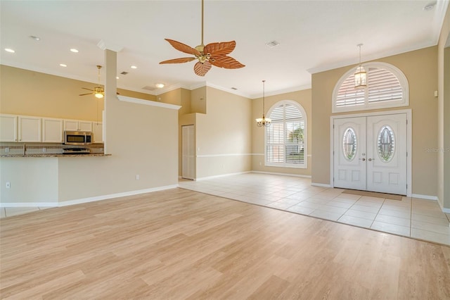 entrance foyer with crown molding, a towering ceiling, ceiling fan with notable chandelier, and light wood-type flooring