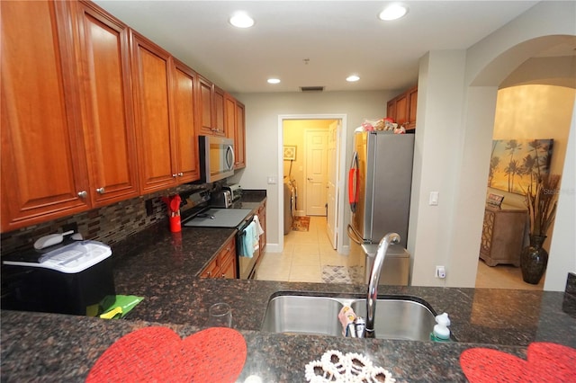 kitchen with tasteful backsplash, dark stone countertops, light tile patterned floors, and stainless steel appliances