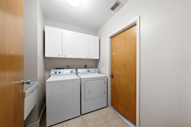 laundry room with cabinets, independent washer and dryer, a textured ceiling, and light tile patterned floors