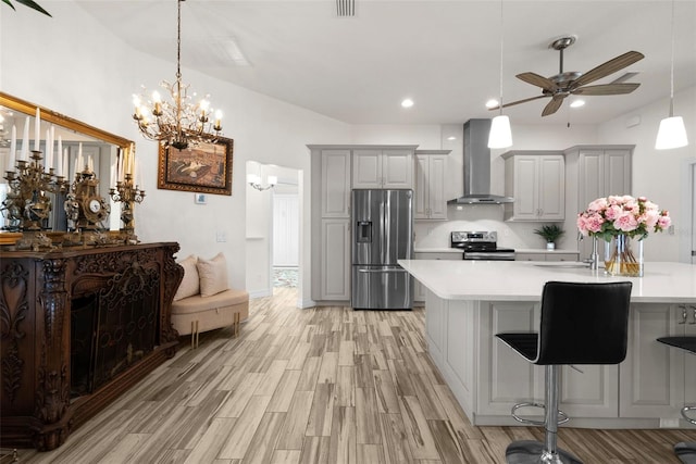 kitchen with pendant lighting, a breakfast bar area, stainless steel appliances, wall chimney range hood, and light wood-type flooring