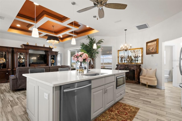 kitchen featuring coffered ceiling, sink, light hardwood / wood-style flooring, appliances with stainless steel finishes, and an island with sink