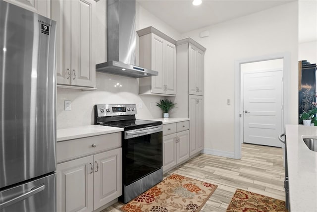 kitchen featuring light hardwood / wood-style flooring, appliances with stainless steel finishes, gray cabinetry, tasteful backsplash, and wall chimney exhaust hood