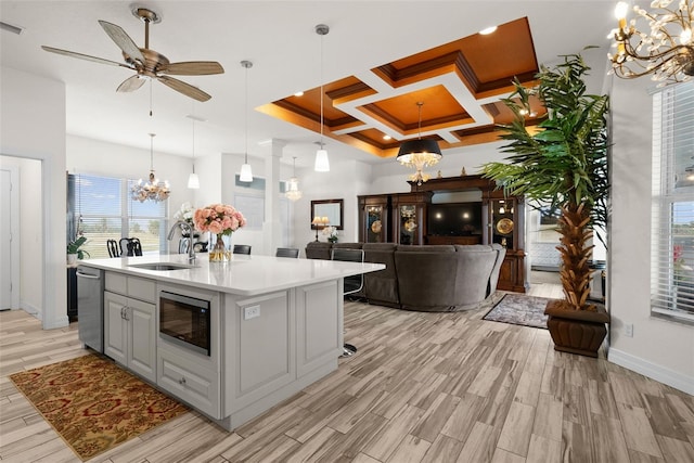 kitchen with built in microwave, an island with sink, sink, and hanging light fixtures