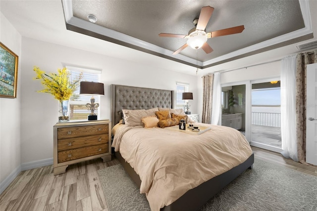 bedroom with crown molding, a textured ceiling, access to outside, a tray ceiling, and ceiling fan