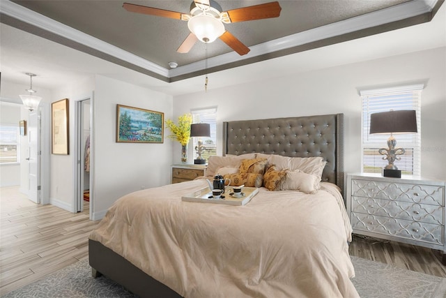 bedroom with crown molding, hardwood / wood-style floors, ceiling fan, and a tray ceiling