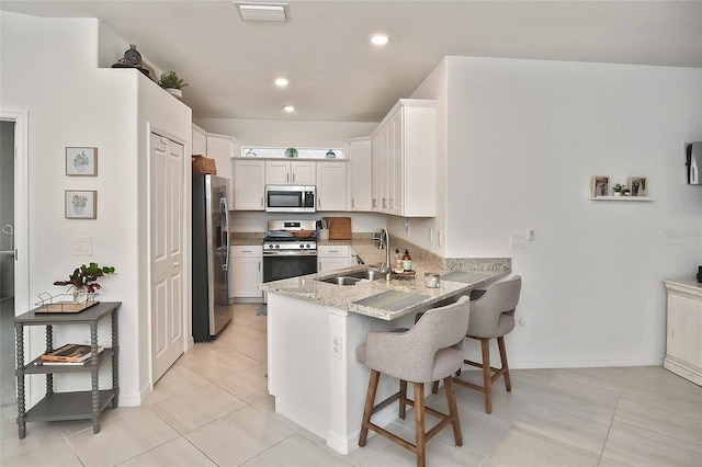 kitchen with a kitchen breakfast bar, sink, light tile patterned floors, white cabinetry, and stainless steel appliances