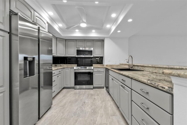 kitchen with gray cabinetry, light stone countertops, sink, stainless steel appliances, and a tray ceiling