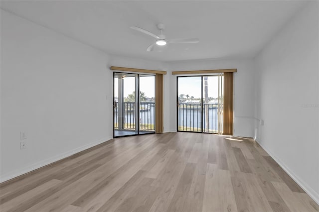 empty room with ceiling fan, a water view, and light wood-type flooring