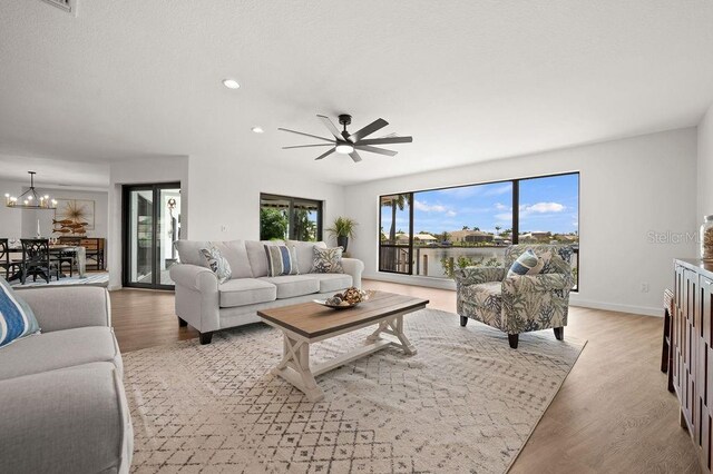 living room featuring ceiling fan with notable chandelier and light hardwood / wood-style flooring