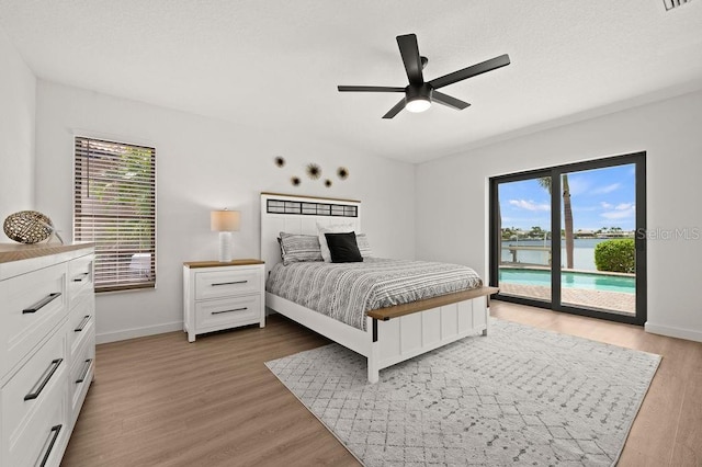 bedroom featuring access to exterior, a water view, ceiling fan, and dark hardwood / wood-style flooring