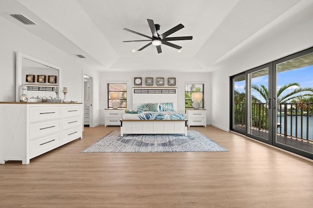 bedroom featuring access to outside, light hardwood / wood-style floors, ceiling fan, and a raised ceiling