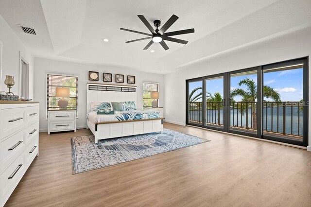 bedroom with ceiling fan, access to outside, multiple windows, a water view, and a tray ceiling