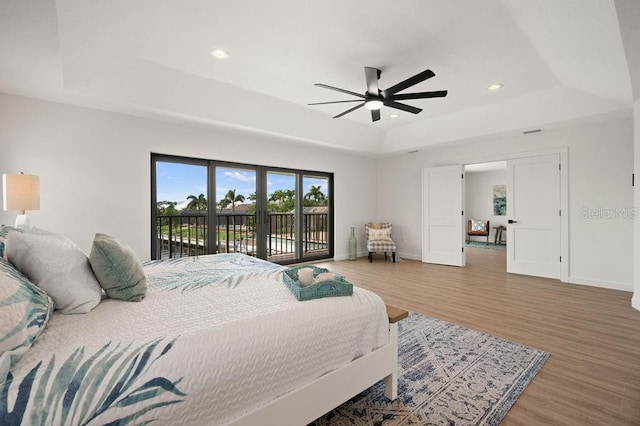 bedroom with access to exterior, a raised ceiling, hardwood / wood-style floors, and ceiling fan