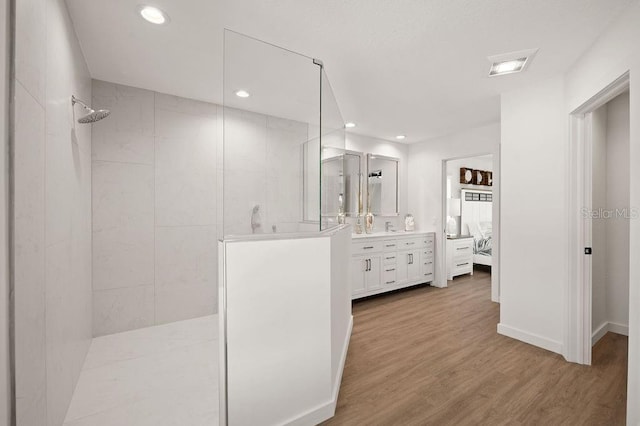 bathroom featuring wood-type flooring, a tile shower, and vanity