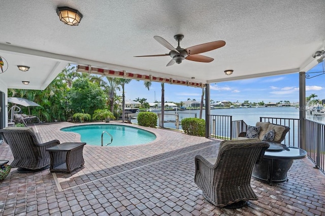 view of swimming pool featuring ceiling fan, a patio area, and a water view