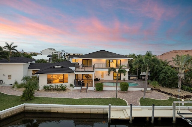 back house at dusk with a patio, a balcony, and a yard