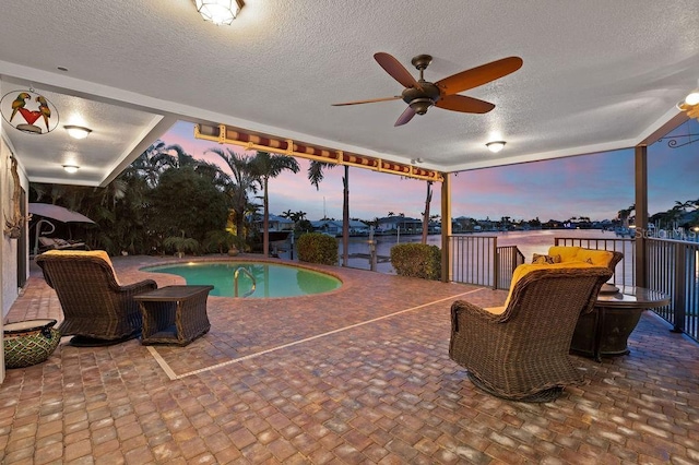 pool at dusk featuring ceiling fan, a water view, and a patio area