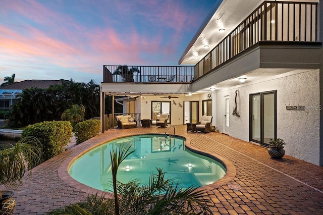 pool at dusk with ceiling fan, a patio area, and an outdoor hangout area