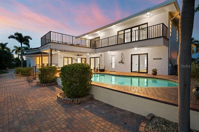 back house at dusk with a balcony, a patio area, and ceiling fan