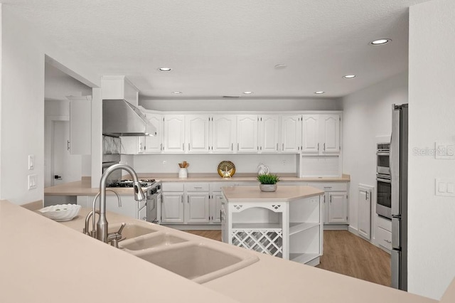 kitchen featuring stainless steel stove, wall chimney exhaust hood, white cabinets, and light wood-type flooring