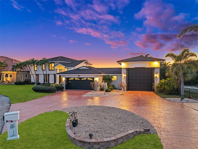 prairie-style home with a garage, a front lawn, decorative driveway, and stucco siding