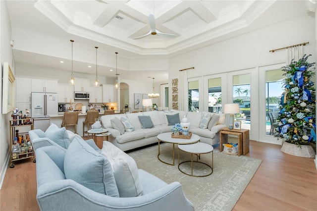 living room with ceiling fan with notable chandelier, a towering ceiling, light wood-type flooring, and coffered ceiling